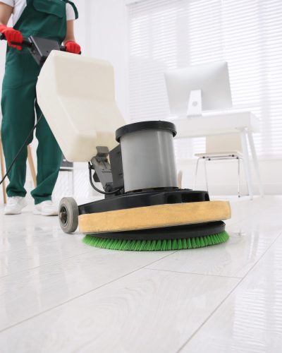 Professional janitor cleaning parquet floor with polishing machine in office, closeup